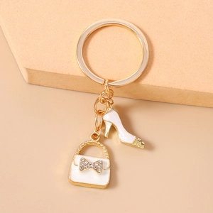Detailed close-up of a gold keychain featuring a white stiletto shoe and a rhinestone bow bag