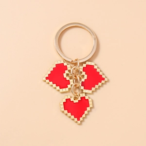 Macro detail of gold keychain with three red pixel heart charms on a warm background