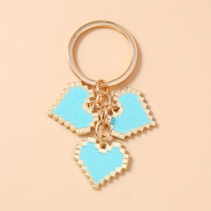 Close-up of golden mosaic pixel heart keychains with blue enamel on pink background