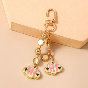 Detailed macro of gold beaded keychain featuring pink enamel cloud charms and HI text