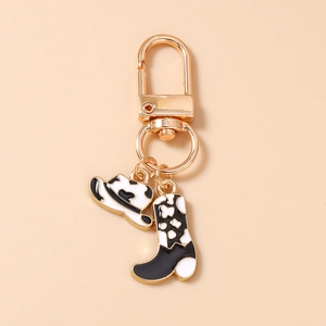 Détail de breloques chapeau et botte de cow-boy émaillés à motif vache sur porte-clés
