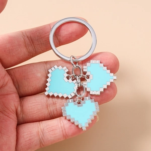 Close-up of three light blue pixel heart keychains held by hand against a pink backdrop