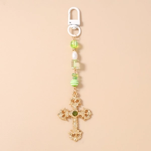 Detail of baroque gold cross keychain with green gemstone and striped beads accent