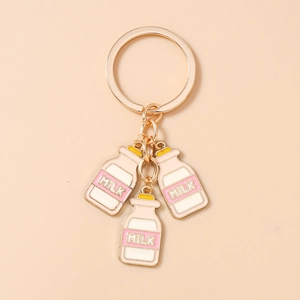 Detail van drie roze en witte melkfles emaille bedeltjes aan een gouden ring