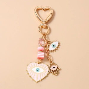 Detailed view of evil eye keychain with heart charms and pink beads on a beige surface
