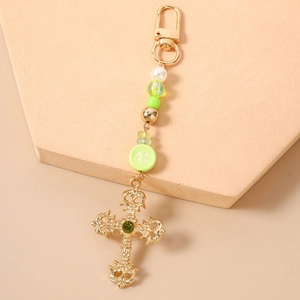 Detailed close-up of a golden hollow cross keychain with green gem and beaded charms