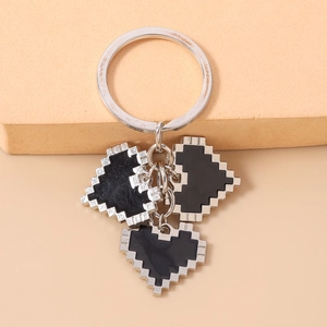 Detail of silver keychain with three black enamel pixel heart charms on a beige surface