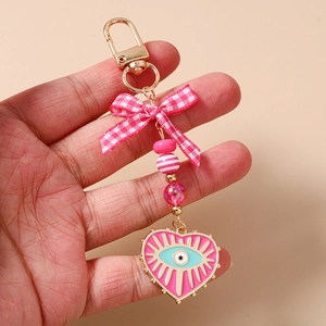 Detail of pink bow and beaded heart keychain with evil eye charm on golden metal clip