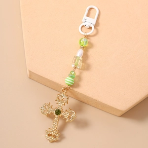 Detail of beaded keychain with cross pendant, green rhinestones, and striped beads on pink base