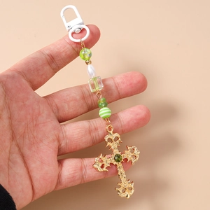 Close-up of a vintage golden cross keychain with green beads and a white clasp