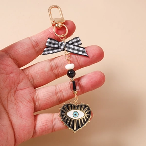 Detail of beaded evil eye keychain with black plaid bow and golden heart charm on hand