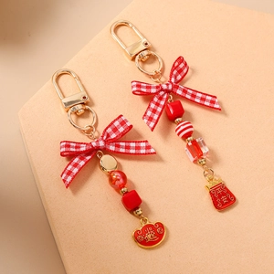 Detail of red beaded keychain with plaid bow and gold lobster clasp featuring lucky charms