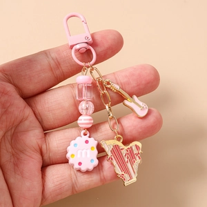 Detailed shot of pink beaded keychain with guitar, harp, and cookie charms held in hand