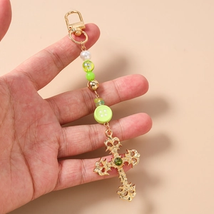 Macro view of ornate gold cross keychain with green gem and beaded stripe strap