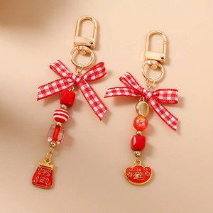 Beaded keychain with red bow and gold metal pendants featuring traditional patterns