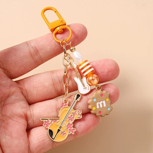 Detail of beaded keychain with violin, guitar, and chocolate cookie pendant on orange carabiner