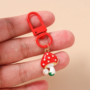 Detail of red mushroom keychain with white pearls and metal lobster clasp held in hand
