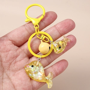 Goldener Delphin Schlüsselanhänger mit Glocke und Glitzer Pailletten in der Hand auf Rosa