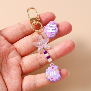 Detail of purple star and cloud keychain with lobster clasp held by hand on beige background