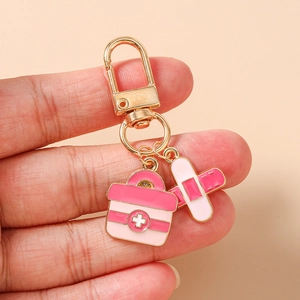 Detail view of medical keychain with pink first aid box and bandage charms held by hand