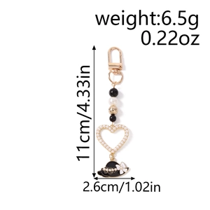 Detail of beaded keychain featuring a pearl heart frame and a black sun hat charm