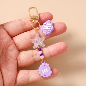 Detail of purple star keychain with beaded charms and cloud pendant held by hand