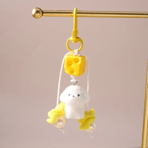 Close-up of white plush puppy keychain with yellow cheese accessory and pearls