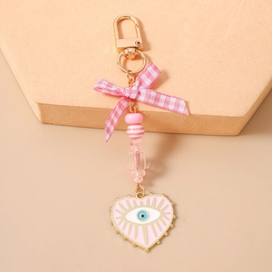 Detail of pink bow and beaded heart keychain with evil eye charm and gold lobster clasp