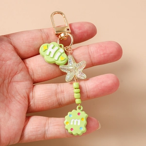 Close-up of a mint green cloud and starfish keychain held by hand on beige background
