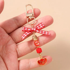 Close-up of beaded keychain with red bow and gold heart pendant against orange background