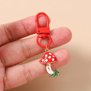 Close-up of a red spotted mushroom keychain with green leaves and a red metal clasp