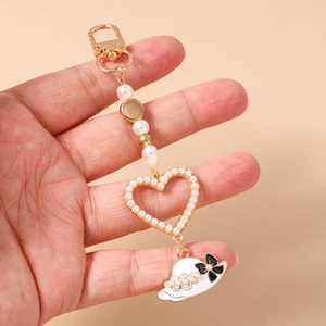 Detail of beaded keychain featuring a gold clasp, pearl heart pendant, and enamel sun hat