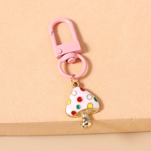 Close-up of a white enamel mushroom keychain with colorful dots and golden metal finish