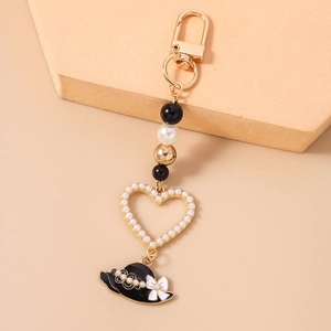 Detail of heart-shaped pearl keychain with golden D-ring and black sun hat charm