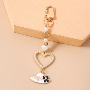 Close-up of golden keychain with pearls, heart pendant and white enamel hat charm