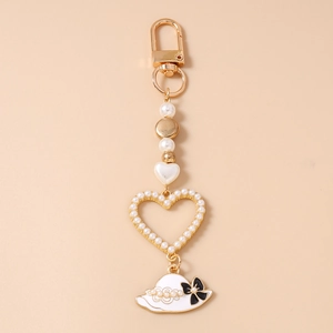 Detail of keychain featuring white pearls, large heart frame and sun hat with black bow