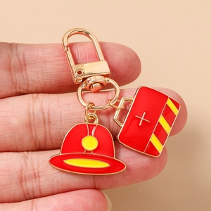 Detail view of gold keychain with red fire helmet and medical kit charms held in hand