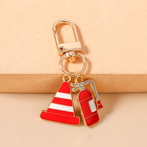 Detailed close-up of metal fire extinguisher and traffic cone enamel charms on a gold keychain