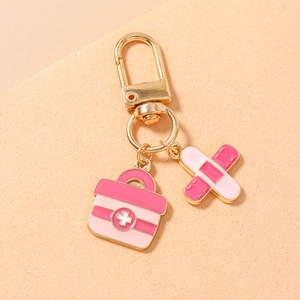 Detail of creative gold keychain with pink medical box and band-aid enamel charms