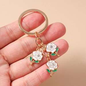 Close-up of golden keychain with white enamel camellia flowers and sparkling rhinestones