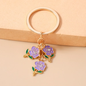 Close-up of golden keychain featuring three purple enamel roses with crystal centers