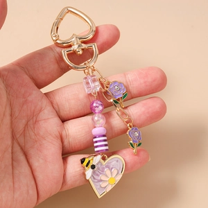 Dettaglio del portachiavi a cuore con api e rose viola con ciondoli a perline in mano