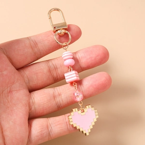 Detail of a pixel heart keychain featuring pink beads and a gold metal clasp held in hand