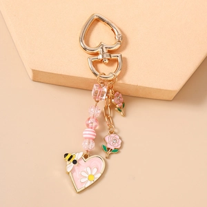 Dettaglio dei ciondoli a rosa rosa e cuore con ape su portachiavi dorato raffinato