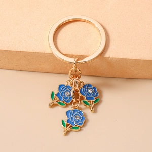Close-up of golden keychain featuring blue enamel roses with crystal center and green leaves