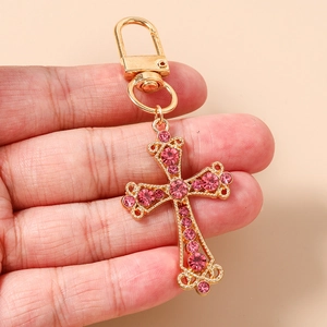 Détail d'un porte-clés croix doré orné de strass roses avec fermoir à ressort en main