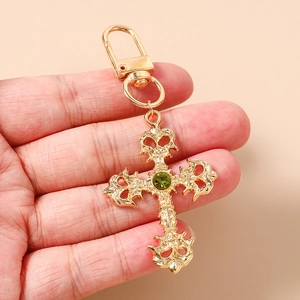 Détail d'un porte-clés croix gothique dorée avec des strass verts et motifs ajourés