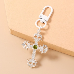 Détail macro d'un porte-clés croix argentée avec strass vert sur un support en pierre