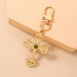Détail d'un porte-clés croix dorée vintage avec pierre verte sur un support en pierre