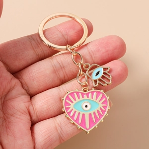 Détail de breloques cœur en émail rose œil bleu et main de hamsa sur porte-clés doré
